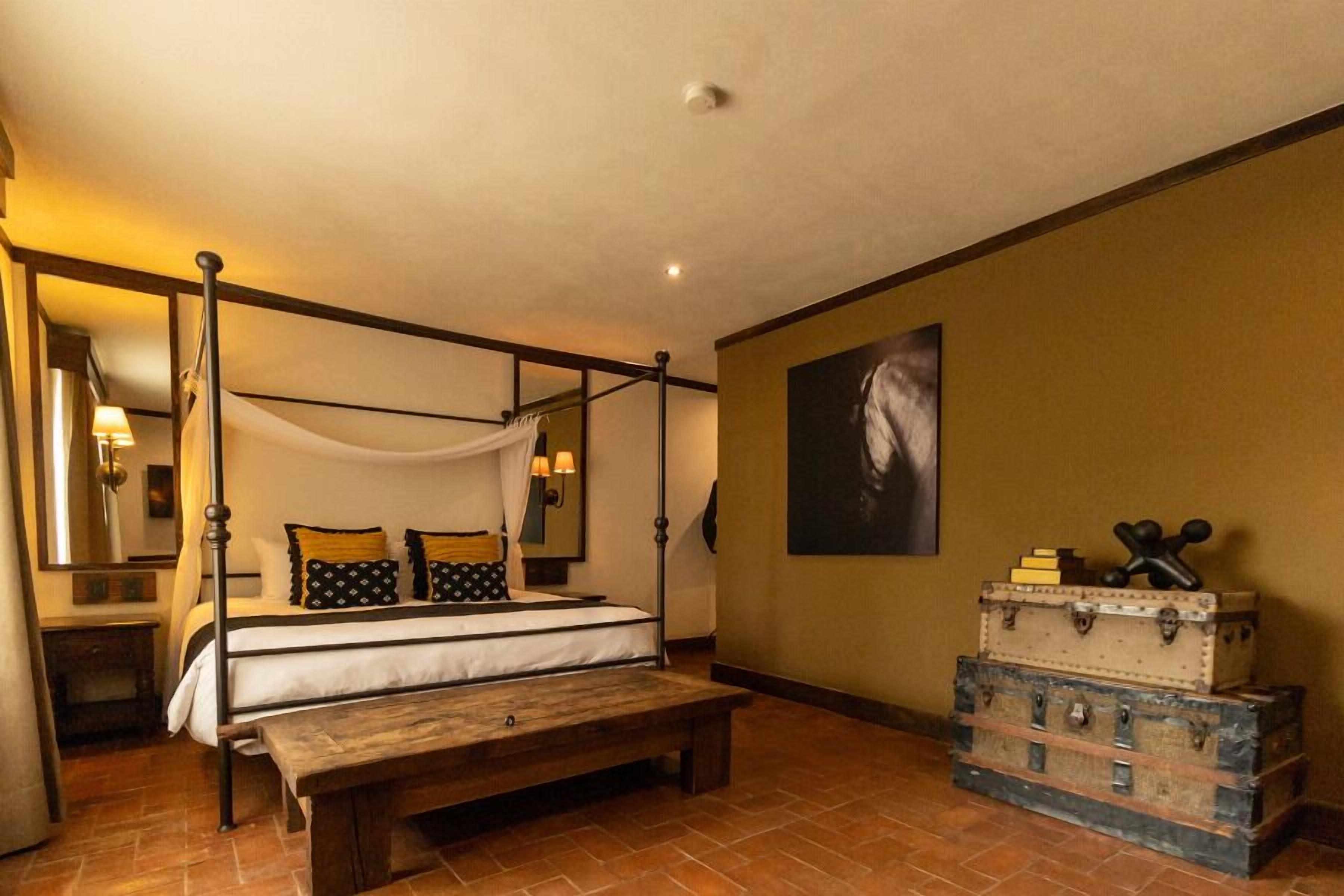 A four-poster bed with a canopy, a wooden bench, and a stack of vintage suitcases.