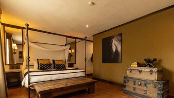 A four-poster bed with a canopy, a wooden bench, and a stack of vintage suitcases.