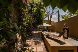 Un espacio al aire libre iluminado por el sol con piscina, sillas de descanso y una pérgola cubierta de enredaderas con flores.