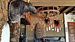 Un interior rústico con pared de piedra, cabeza de toro montada y estructura de techo de madera.