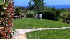 Un jardin avec un chemin de pierres menant à une pelouse, un banc et un grand tonneau.
