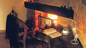 Une pièce chaleureuse avec une cheminée, un fauteuil, une table avec un livre, une tasse de café et un chandelier.