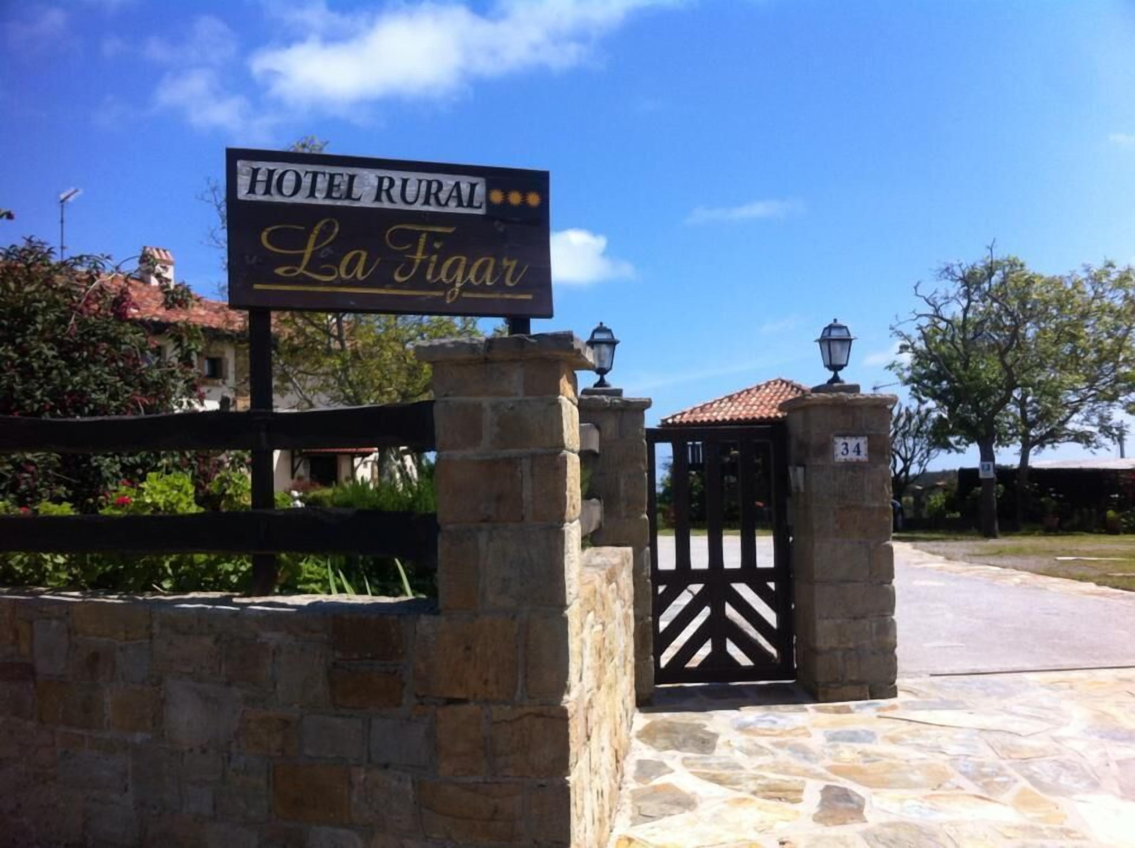 A stone wall with a gate and a sign for Hotel Rural La Figuar.
