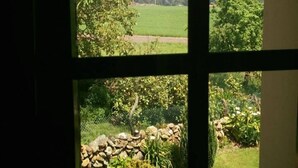 Une vue à travers une fenêtre donnant sur un mur de pierre et un petit jardin.
