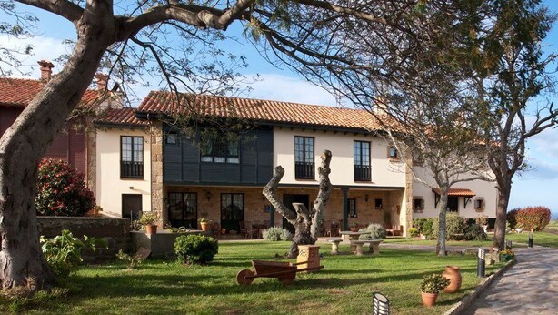 Une villa de style traditionnel, avec un toit en tuiles, une façade en pierre et un jardin bien entretenu agrémenté de plantes en pot et d’un chemin menant à l’entrée.