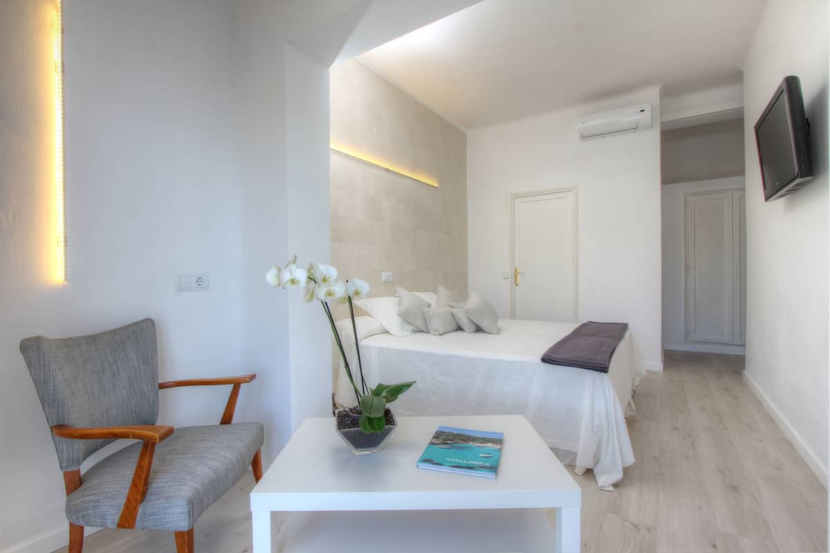 Un dormitorio con una cama, una silla, una mesa con un libro y una planta en maceta.