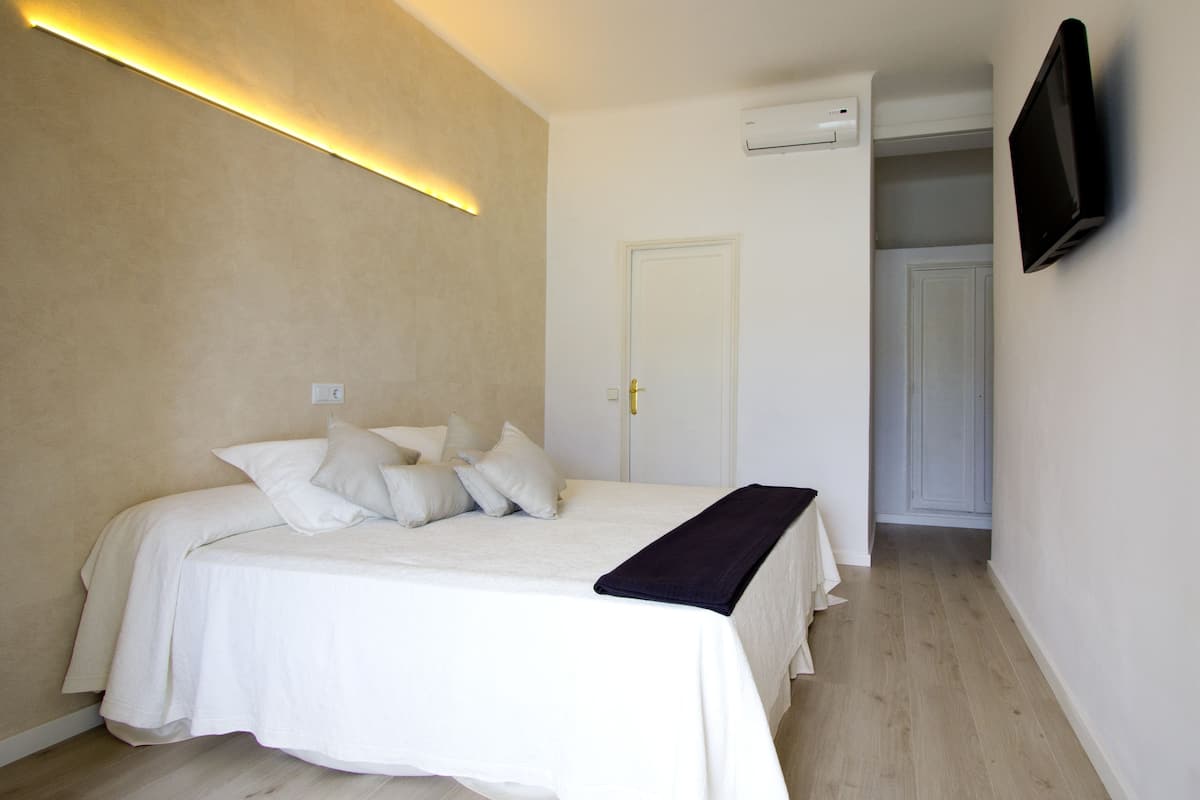 Un dormitorio con cama, una mesita de noche, un televisor de pantalla plana montado en la pared y un equipo de aire acondicionado.