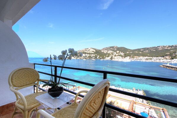 A balcony with wicker chairs and a table, overlooking a coastal town and clear blue sea. - Hotel Brismar (Andraitx)