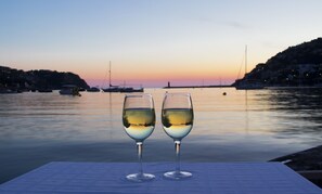 Two wine glasses on a table with a view of a calm harbor at sunset. - Hotel Brismar (Andraitx)