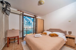 Un dormitorio con una cama grande, una silla, una mesita de noche y vistas a un paisaje montañoso a través de una puerta corredera.