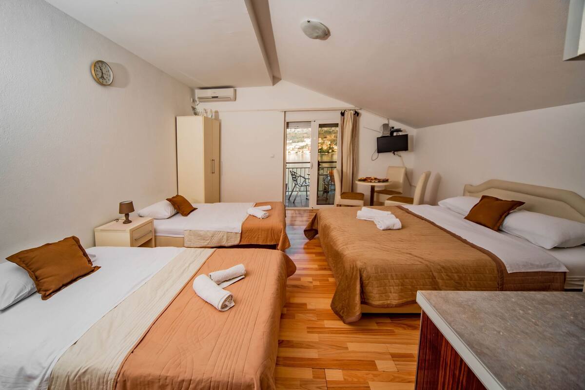 A hotel room with two beds, a small table, a chair, a TV, and a balcony with a view.