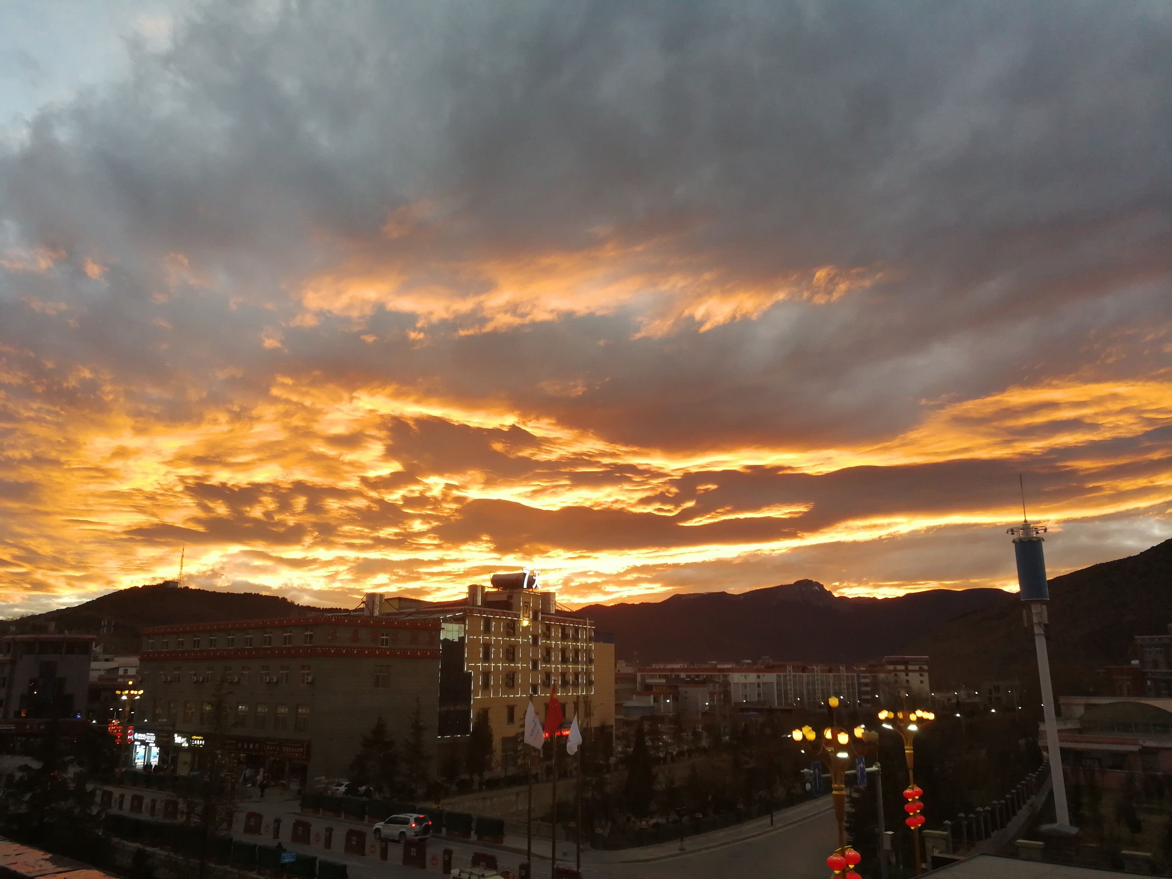 A cityscape with a prominent building featuring a tower, surrounded by other structures and a mountainous backdrop.