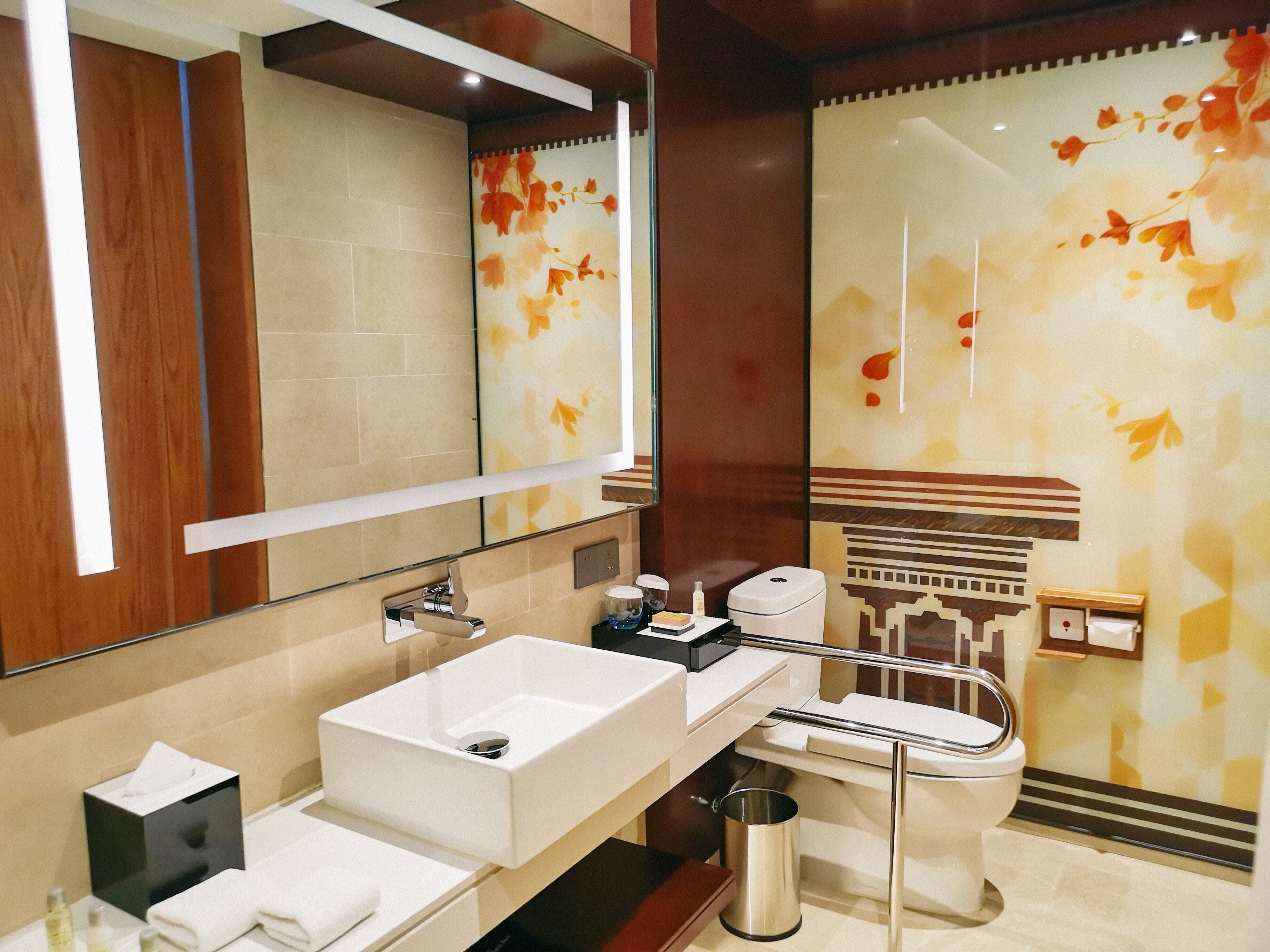 Un baño moderno con un espejo grande, un lavamanos blanco, un inodoro y un cubo de basura.