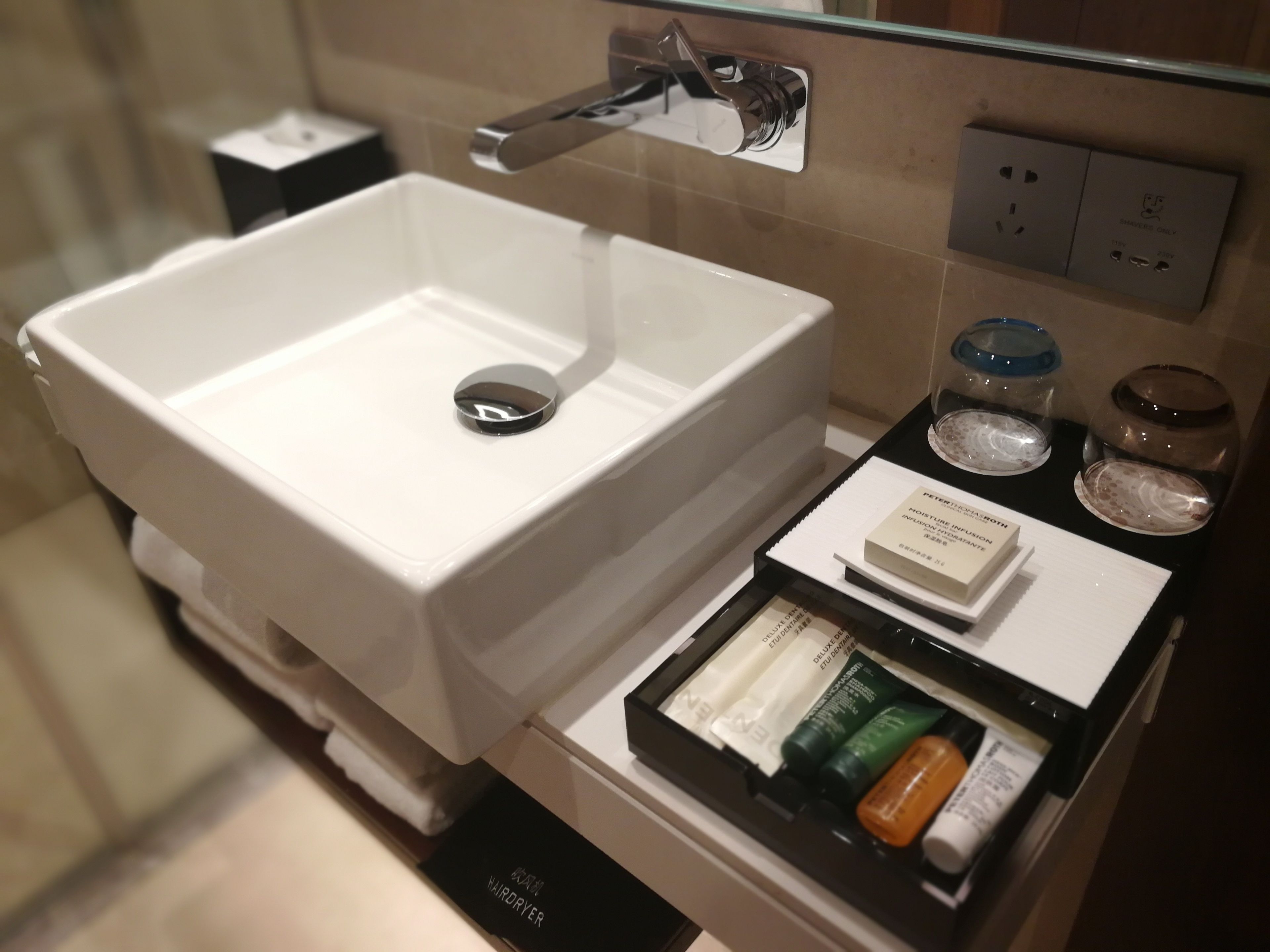 A bathroom with a white sink, a hairdryer, and toiletries.