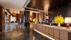 A modern hotel lobby with a reception desk, large pillars, and a staircase. - Hilton Garden Inn Shangri-La (Deqin)