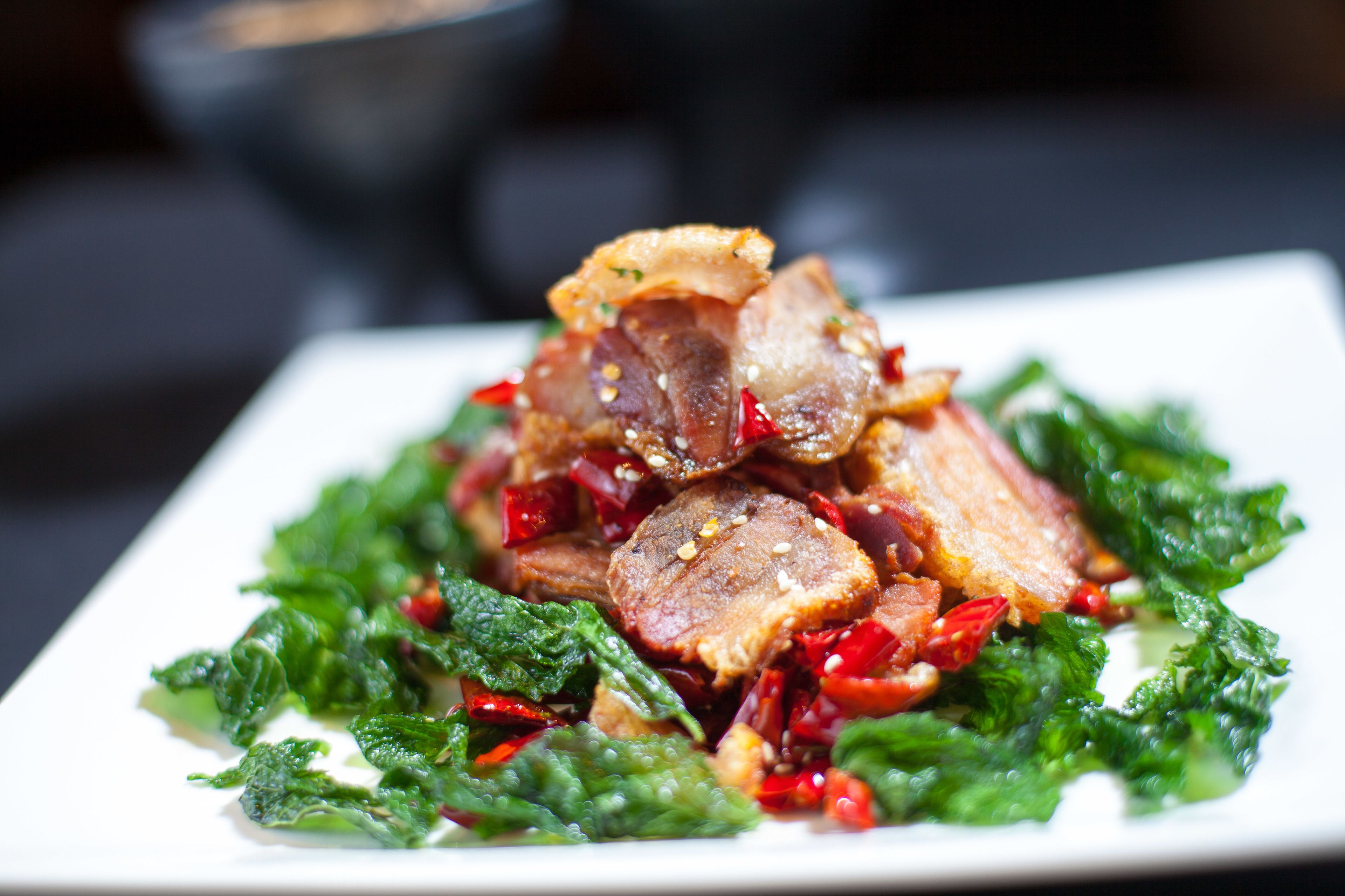 A square plate with a dish of cooked meat and greens.