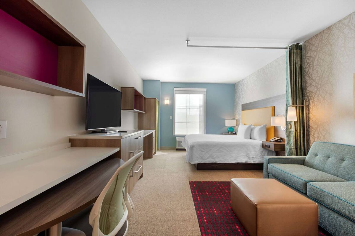 Ett hotellrum med en säng, ett skrivbord med en tv, en soffa och ett fönster.