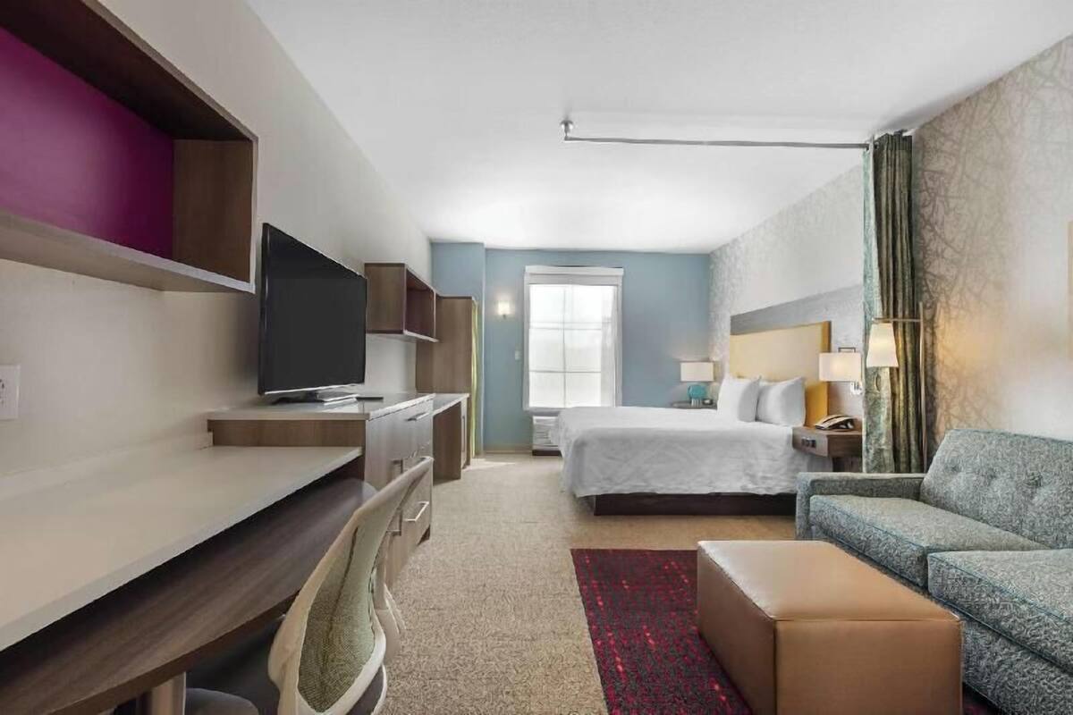 A hotel room with a bed, a sofa, a desk with a TV, a window, and a door.