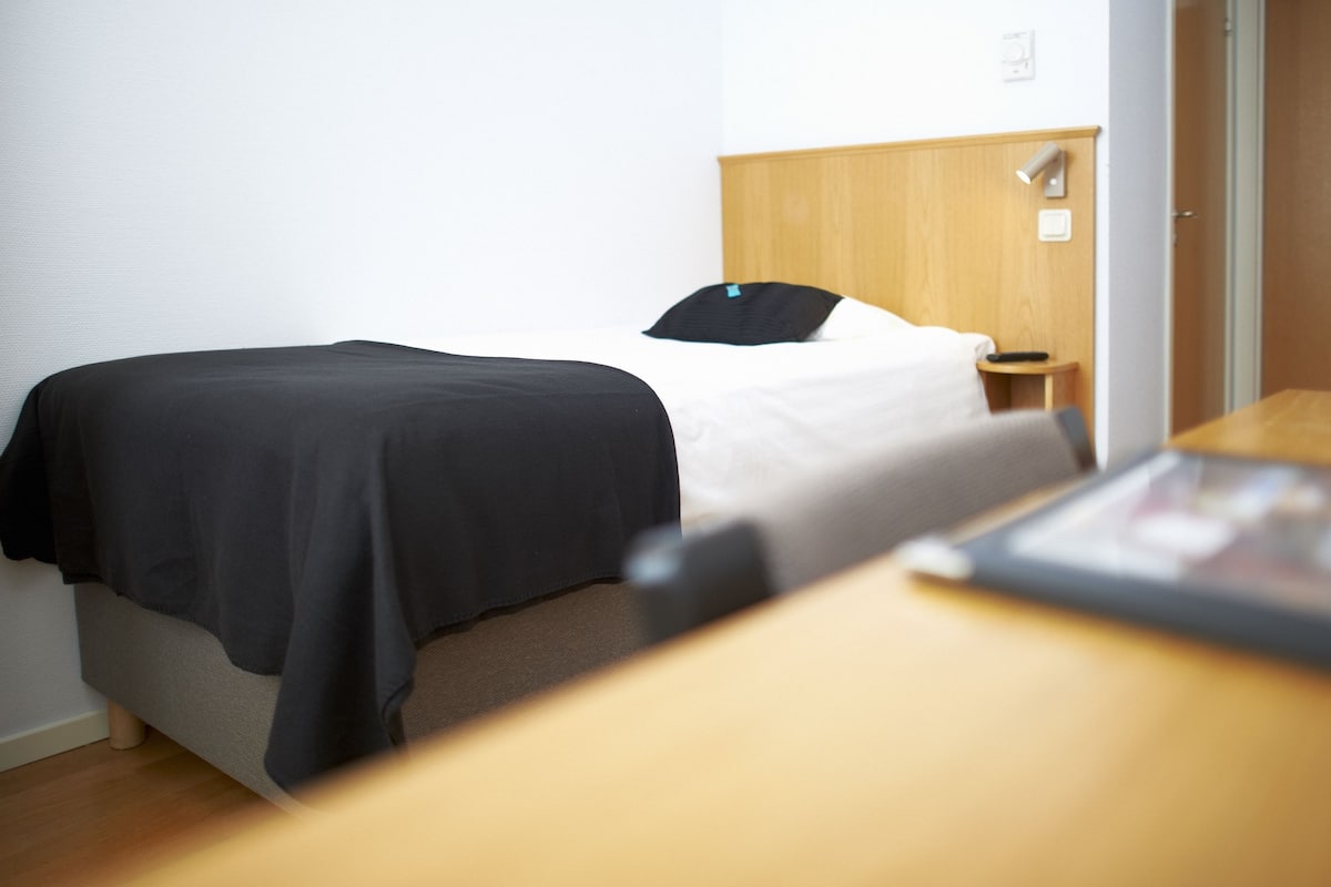 A hotel room with a bed, bedside table, and a wooden headboard.