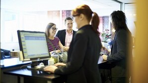 A group of people in a modern office setting with a computer and a coffee cup on the desk. - Hotell Rum Oscar (Oskarshamn)