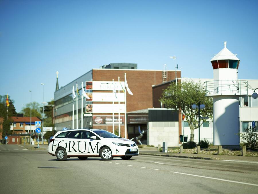 A white car with "FORUM" on the side driving on a road.