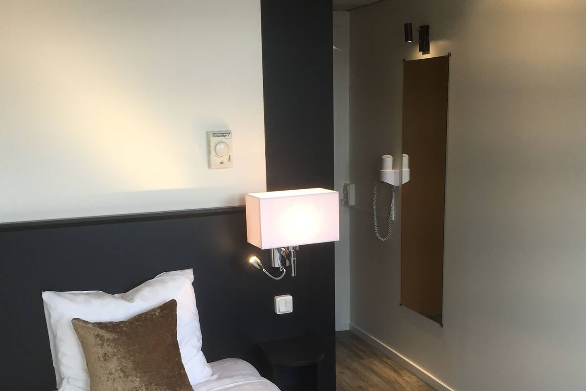 A hotel room with a bed, a nightstand, a wall-mounted phone, and a light fixture.