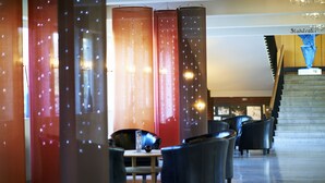 A lobby with a staircase, red and brown pillars, and black leather chairs. - Hotell Rum Oscar (Oskarshamn)