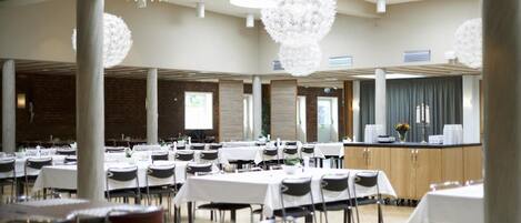 A spacious dining area with round tables, white tablecloths, and modern chandeliers.