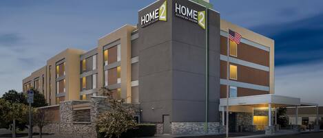 A hotel with a modern design, featuring a prominent 'HOME' sign, a flag, and a covered entrance.