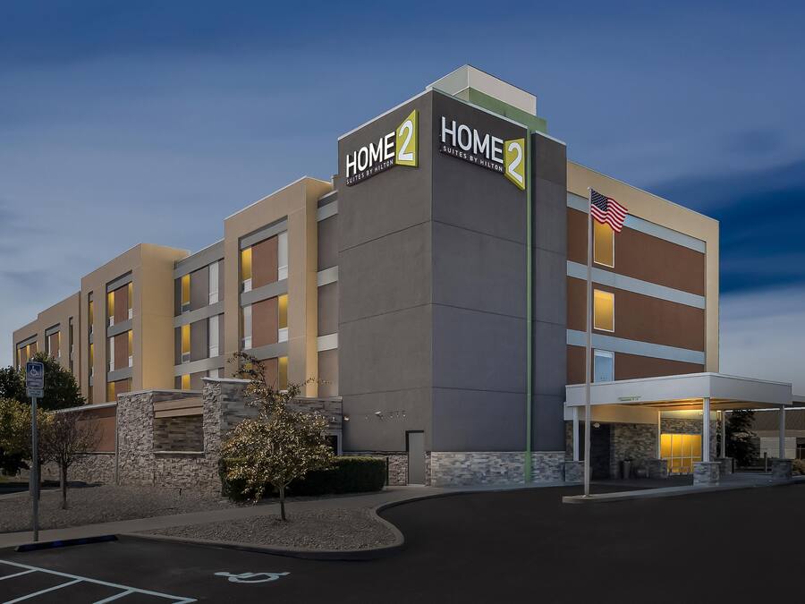 A hotel with a modern design, featuring a prominent 'HOME' sign, a flag, and a covered entrance.