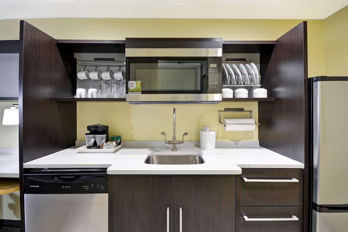 A compact kitchen with a built-in microwave, stainless steel sink, and dark wooden cabinets.