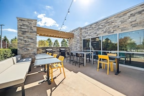 An outdoor patio with tables and chairs, stone walls, and a pergola. - Home2 Suites By Hilton Maumee Toledo (Maumee)