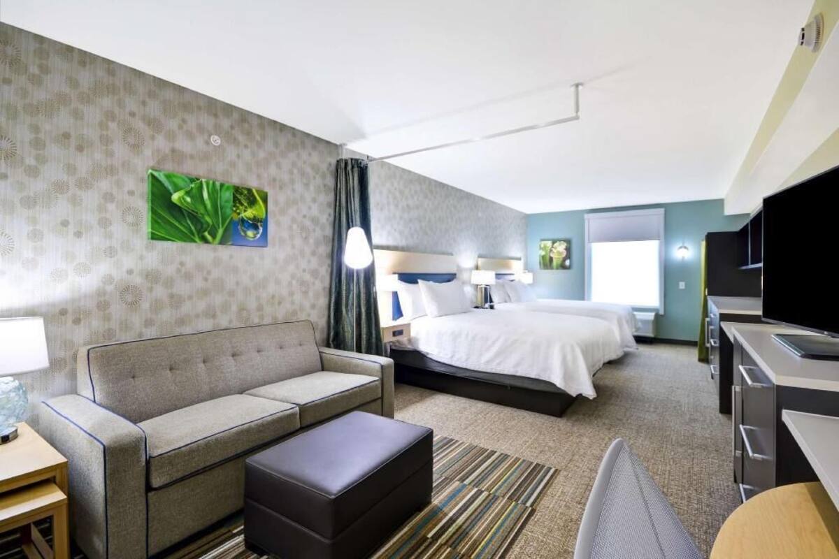 A hotel room with a sofa, a bed, a desk, a television, and a painting on the wall.