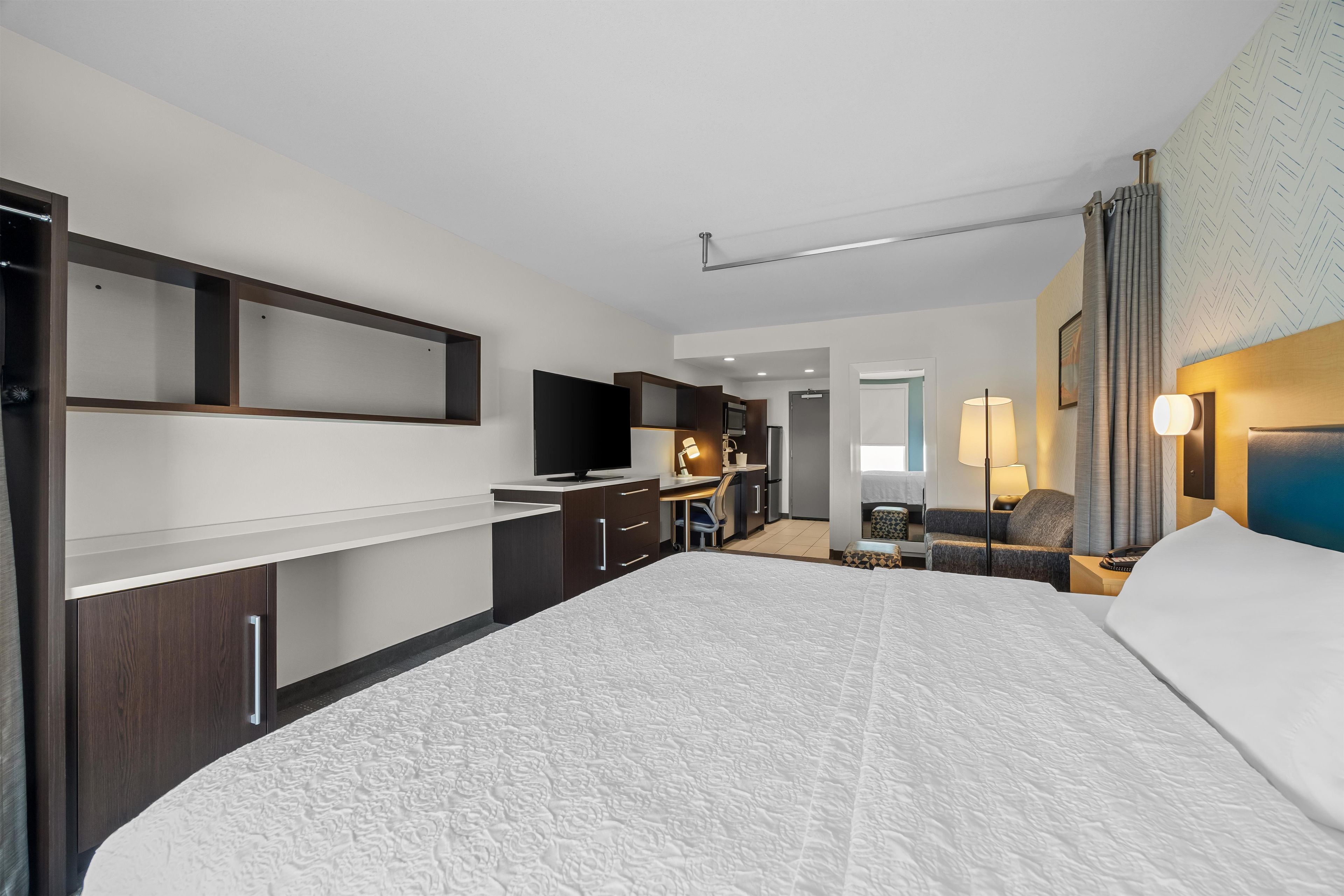 Habitación de hotel con una cama grande, un escritorio con silla, un televisor y una kitchenette.