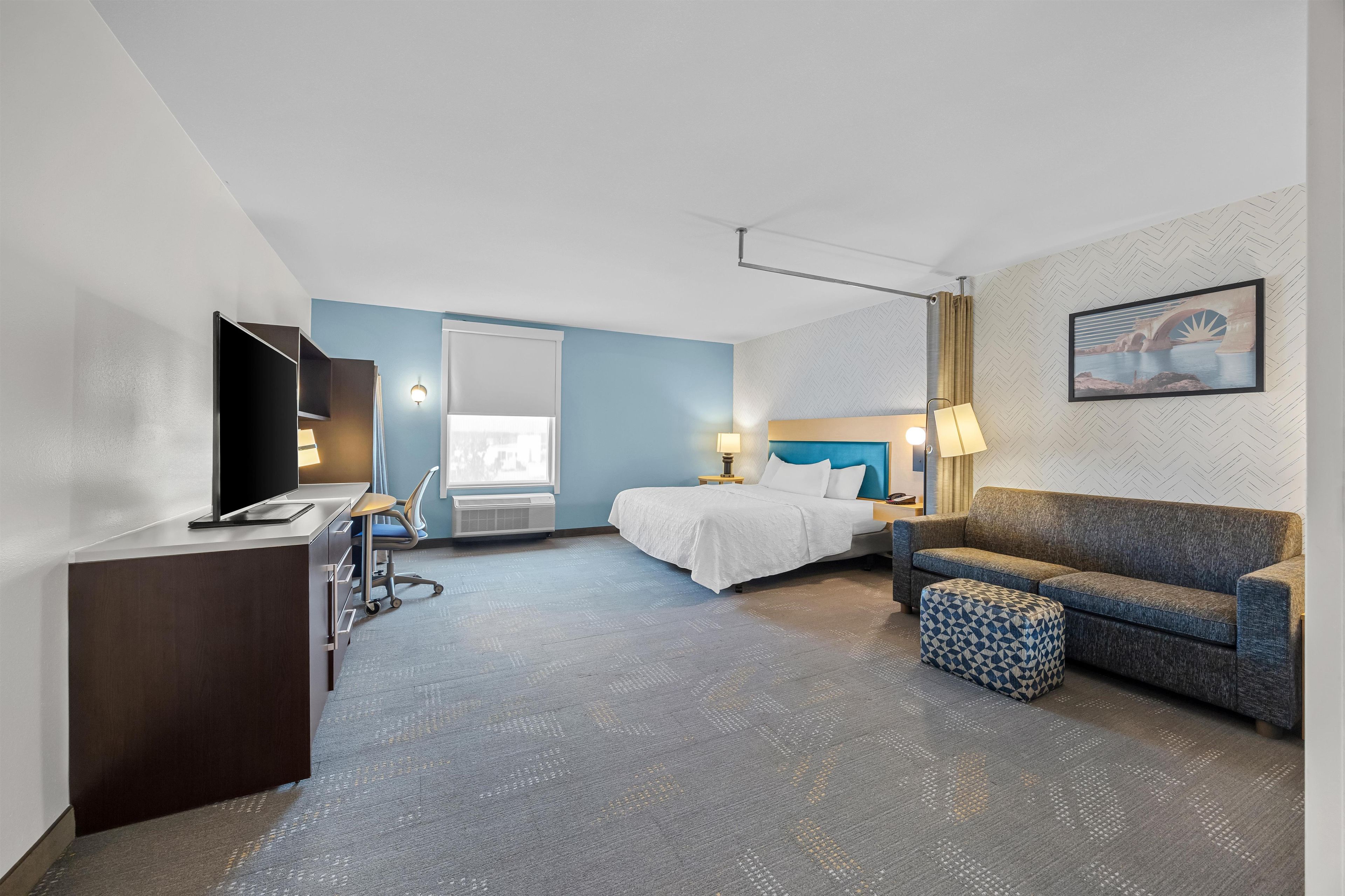 A hotel room with a bed, a desk, a television, a sofa, and a patterned wall.
