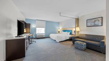 A hotel room with a bed, a desk, a television, a sofa, and a patterned wall.