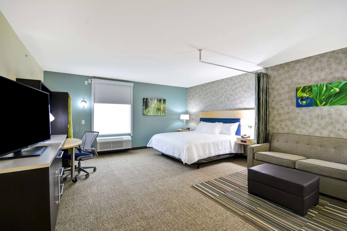 A hotel room with a bed, a sofa, a desk with a TV, and a chair.