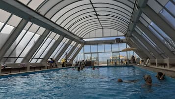 Una piscina techada, una piscina al aire libre, sombrillas