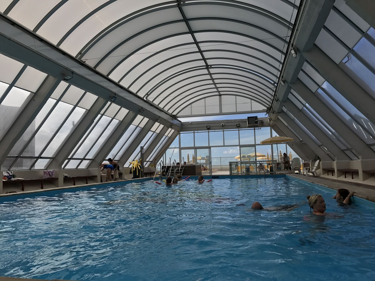 Una piscina cubierta, una piscina al aire libre, sombrillas, tumbonas