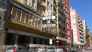 Un edifici de diversos pisos amb balcons, un cartell visible de 'Y & FUERZA' i diversos cotxes aparcats al carrer.