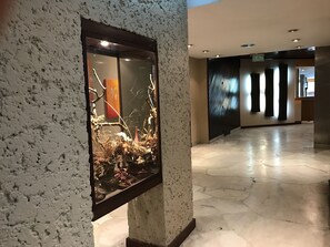Un vestíbulo con una pared texturizada, una vitrina de vidrio con ramas y hojas, y un suelo de baldosas.