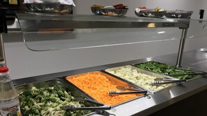 Un bufé con diversas opciones de comida, incluyendo brócoli, zanahorias ralladas, coliflor y verduras de hoja verde.