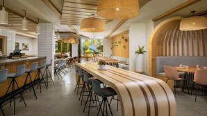Um restaurante moderno com um balcão de madeira comprido, banquetas pretas e uma variedade de opções de assento, incluindo um banco e cadeiras individuais.