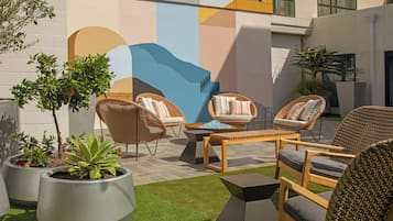 Un área de estar al aire libre con sillas de mimbre, una mesa de madera y macetas con plantas.
