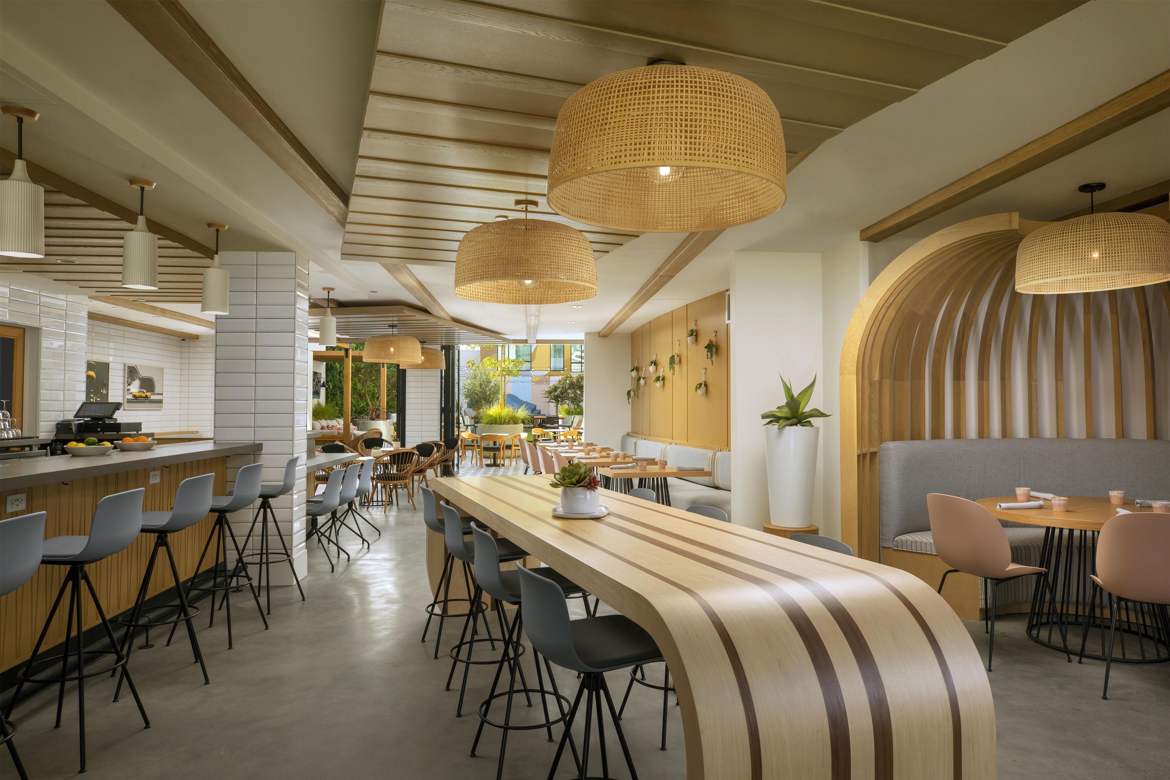 Un restaurante moderno con una barra larga, varias opciones de asientos y luminarias tejidas decorativas.