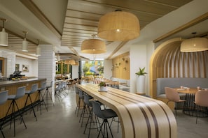 Un interno di un ristorante moderno con un lungo bancone, varie opzioni di posti a sedere e lampade decorative in rattan.