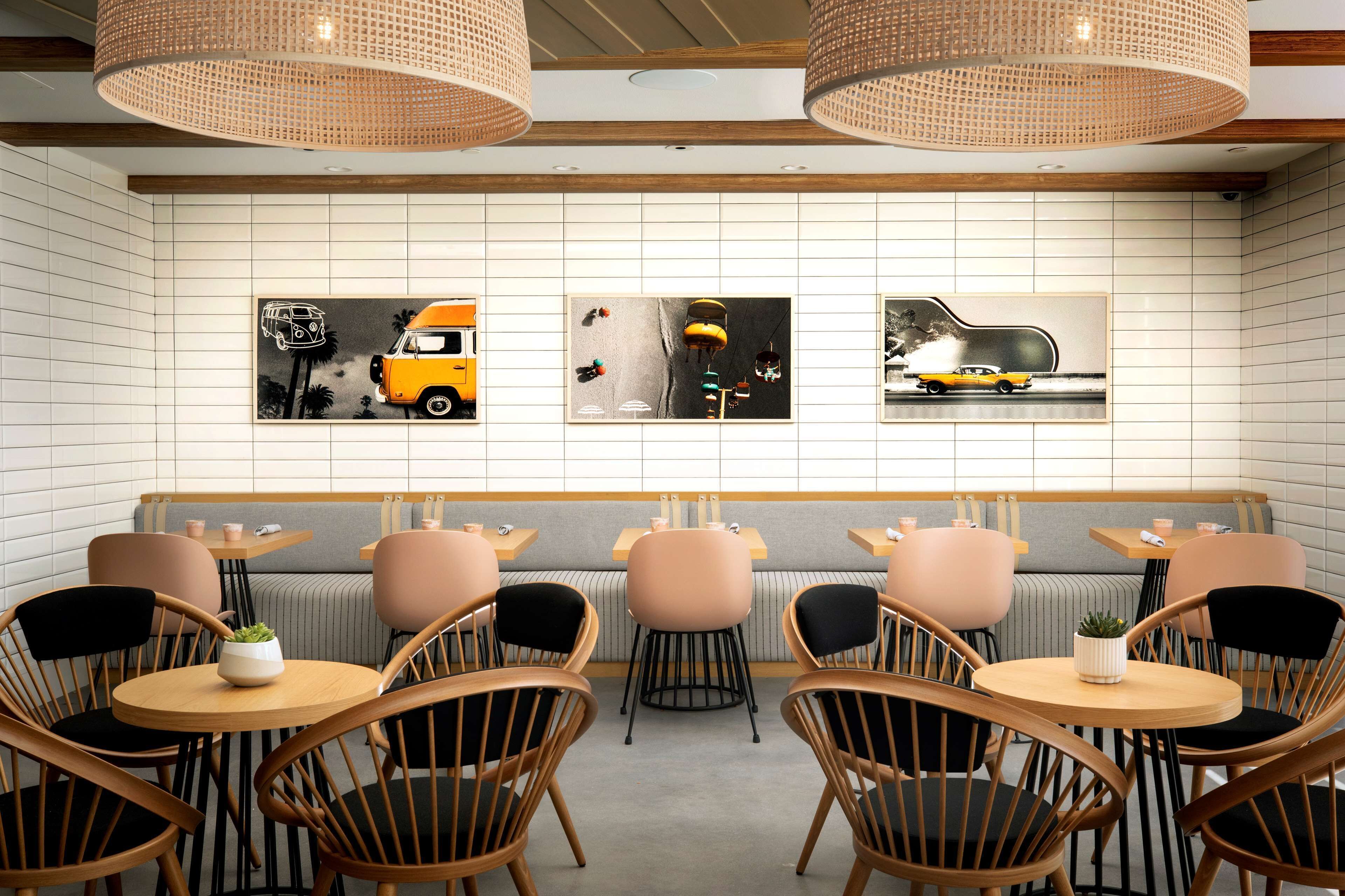 A modern cafe with wooden chairs and tables, a bench, and three wall-mounted artworks depicting vintage cars.
