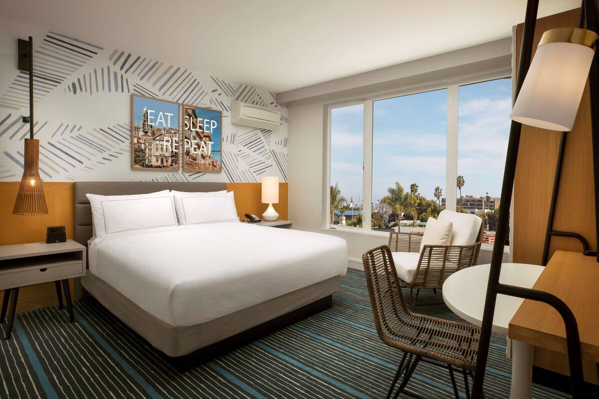 A hotel room with a large bed, a desk, a chair, a table, and a view of the city.