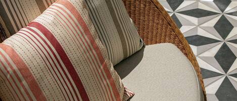 Une chaise en osier avec deux coussins à rayures et un tapis au motif géométrique.