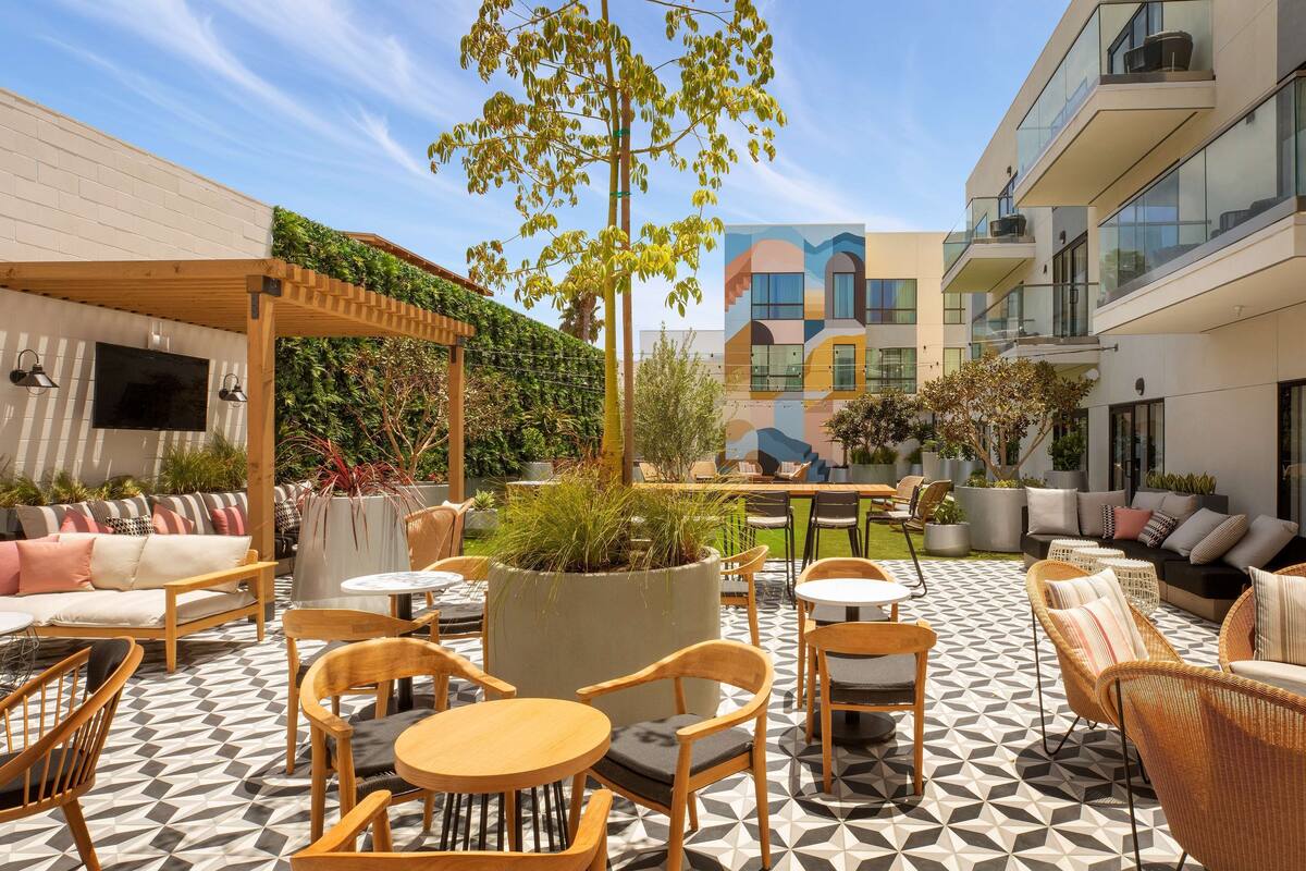 An outdoor patio with wooden furniture, a geometric patterned floor, and a modern building in the background.